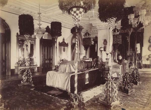 King Kalākaua lying in state, with the pā‘ū of Nāhi‘ena‘ena visible. Queen Kapi‘olani kneeling next to the casket in the Throne Room of ‘Iolani Palace; Honolulu, Hawai‘i. 1891. Collection: General Photograph Collection Call Number: Death. Funerals. Kalākaua, David, 1891. Artifact Number: SP 115953 Location: Bishop Museum Archives Image from Bishop Museum Archives, Honolulu, Hawaii. Images are not to be re-used without permission.