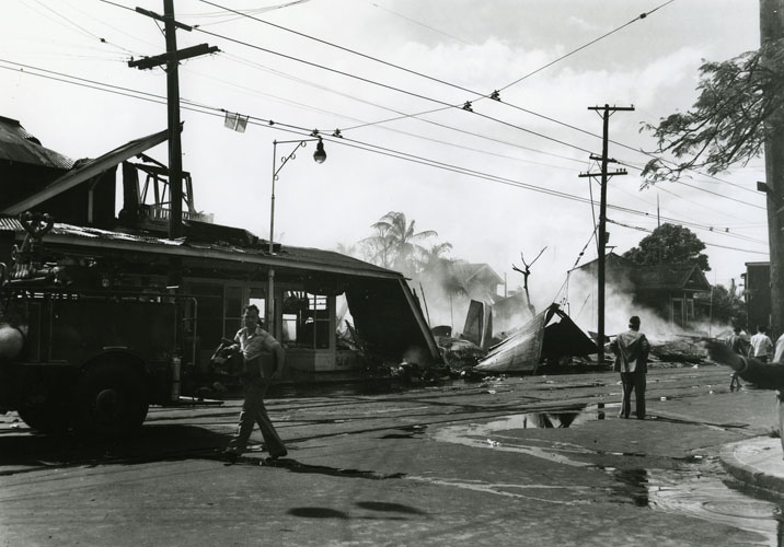 Damaging explosions and fires occurred in multiple locations in Honolulu during the attack on Dec. 7. This photograph shows the area of greatest civilian damage, which was on King Street (in the foreground) at McCully Street. Both stores and houses were destroyed here, and one woman was killed. People naturally believed that bombs from Japanese planes were responsible, but in fact, U.S. Navy anti-aircraft shells that had been fired against the enemy airplanes were the real cause. The shells had not detonated high in the air as they were supposed to, but instead had fallen intact to the ground, where they then blew up. Approximately 60 civilians died on Dec. 7, along with over 3,000 military personnel. Collection: General Photograph Collection Call Number: Military. War. WWII. December 7, 1941 Artifact Number: SP 98512 Location: Bishop Museum Archives Image from Bishop Museum Archives, Honolulu, Hawaii. Images are not to be re-used without permission.
